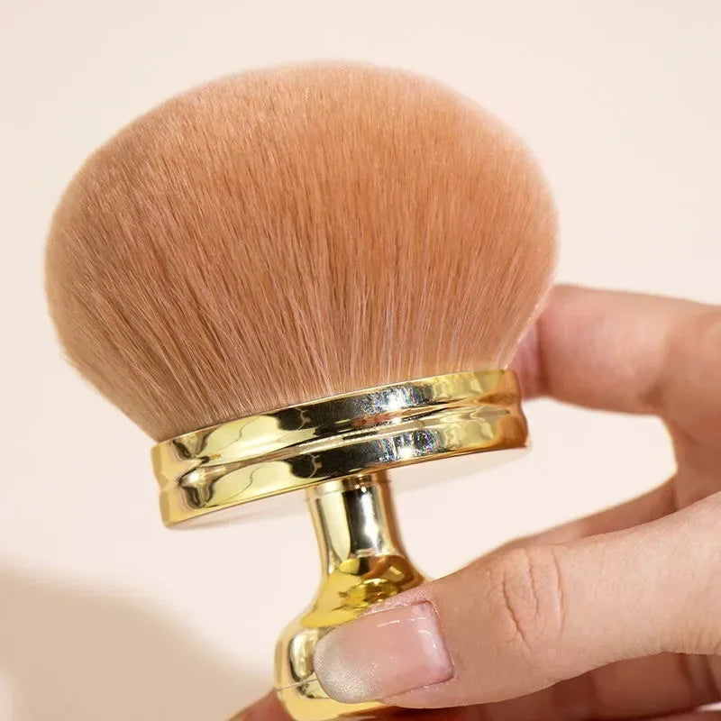 Close-up of a hand holding a fluffy extra large body makeup brush with a gold cap, perfect for applying makeup.