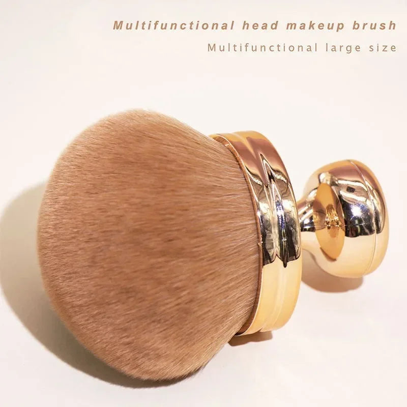 Close-up of a hand holding a fluffy extra large body makeup brush with a gold cap, perfect for applying makeup.