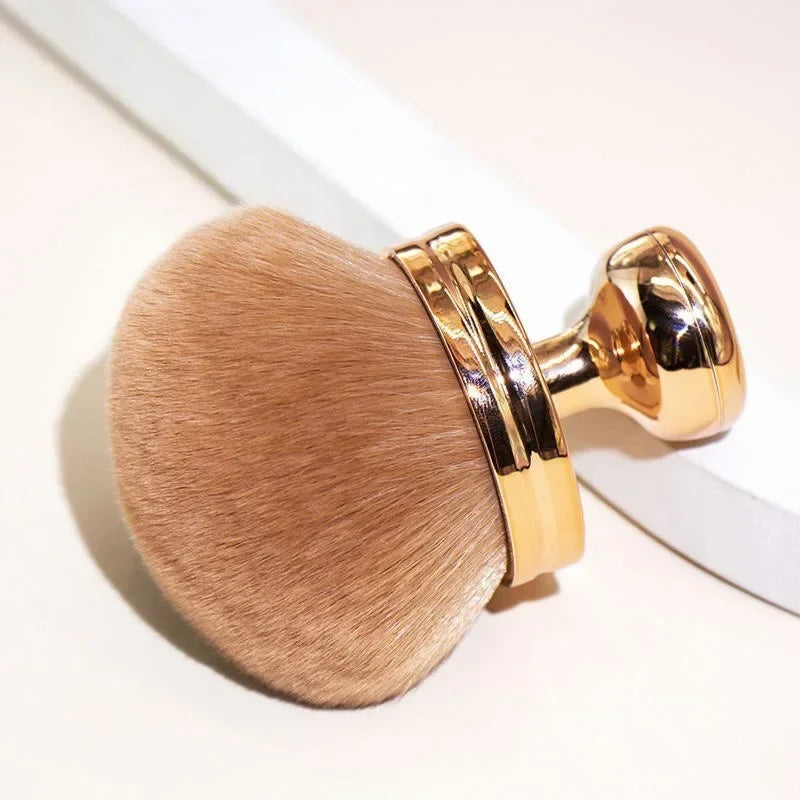 Close-up of a hand holding a fluffy extra large body makeup brush with a gold cap, perfect for applying makeup.