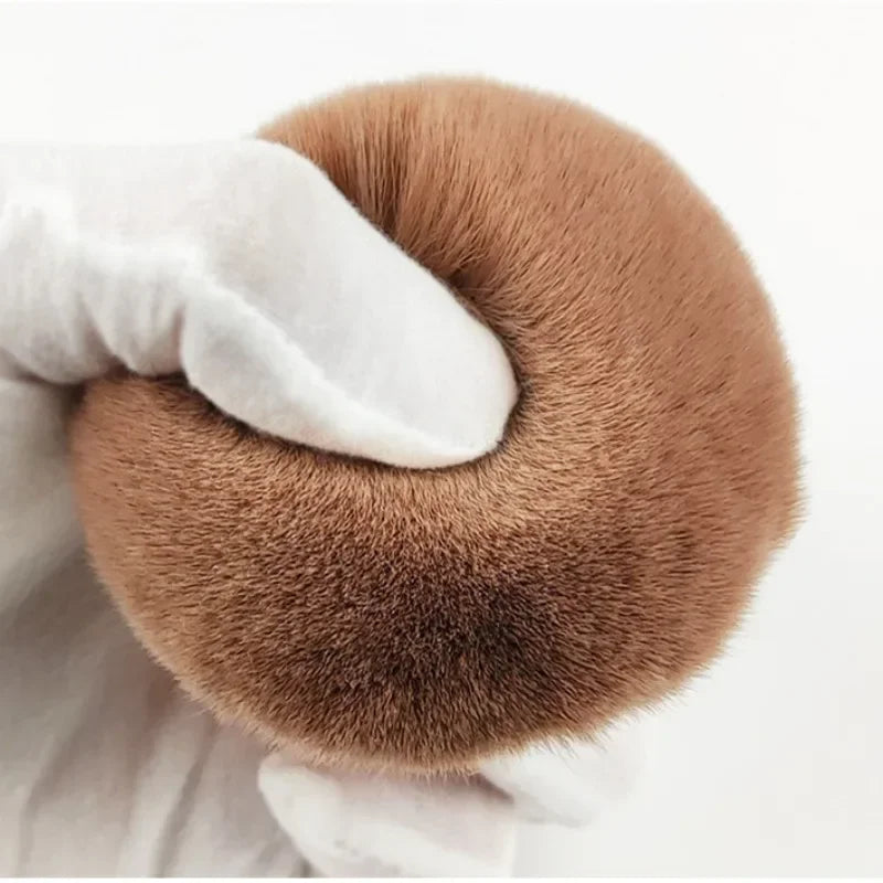 Close-up of a hand holding a fluffy extra large body makeup brush with a gold cap, perfect for applying makeup.