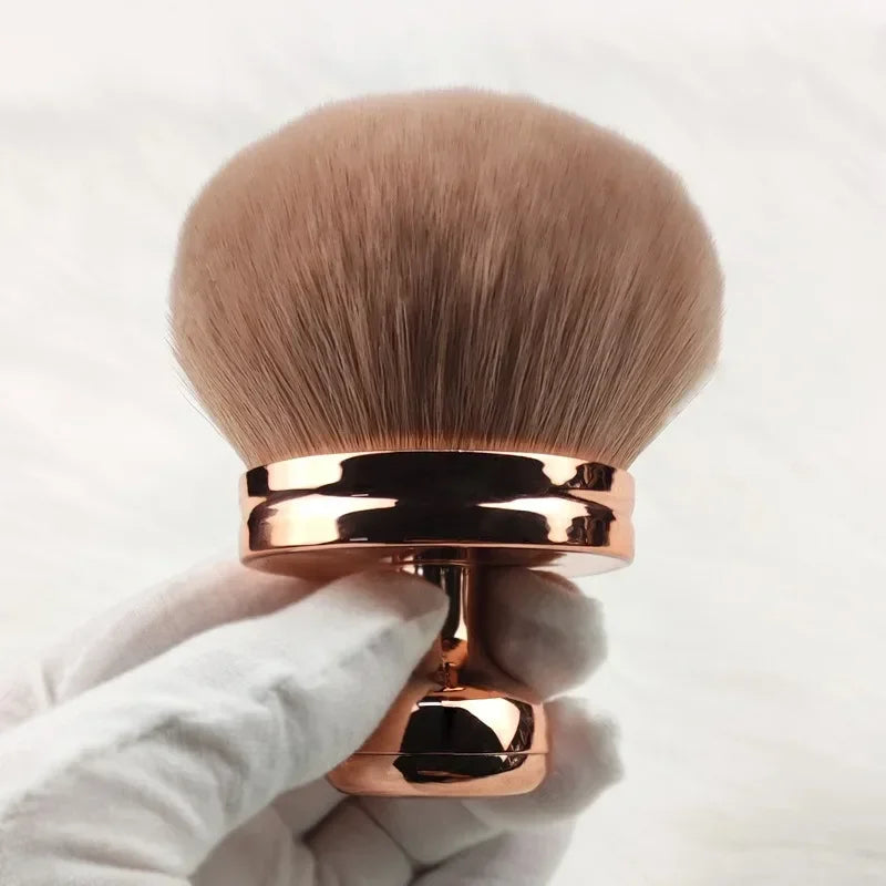 Close-up of a hand holding a fluffy extra large body makeup brush with a gold cap, perfect for applying makeup.