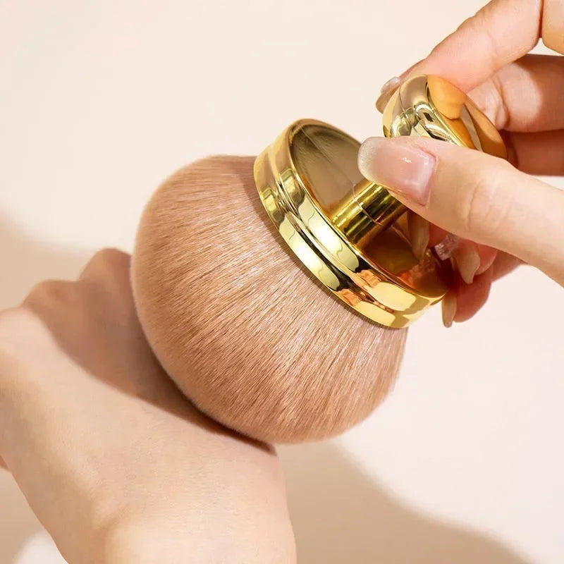 Close-up of a hand holding a fluffy extra large body makeup brush with a gold cap, perfect for applying makeup.