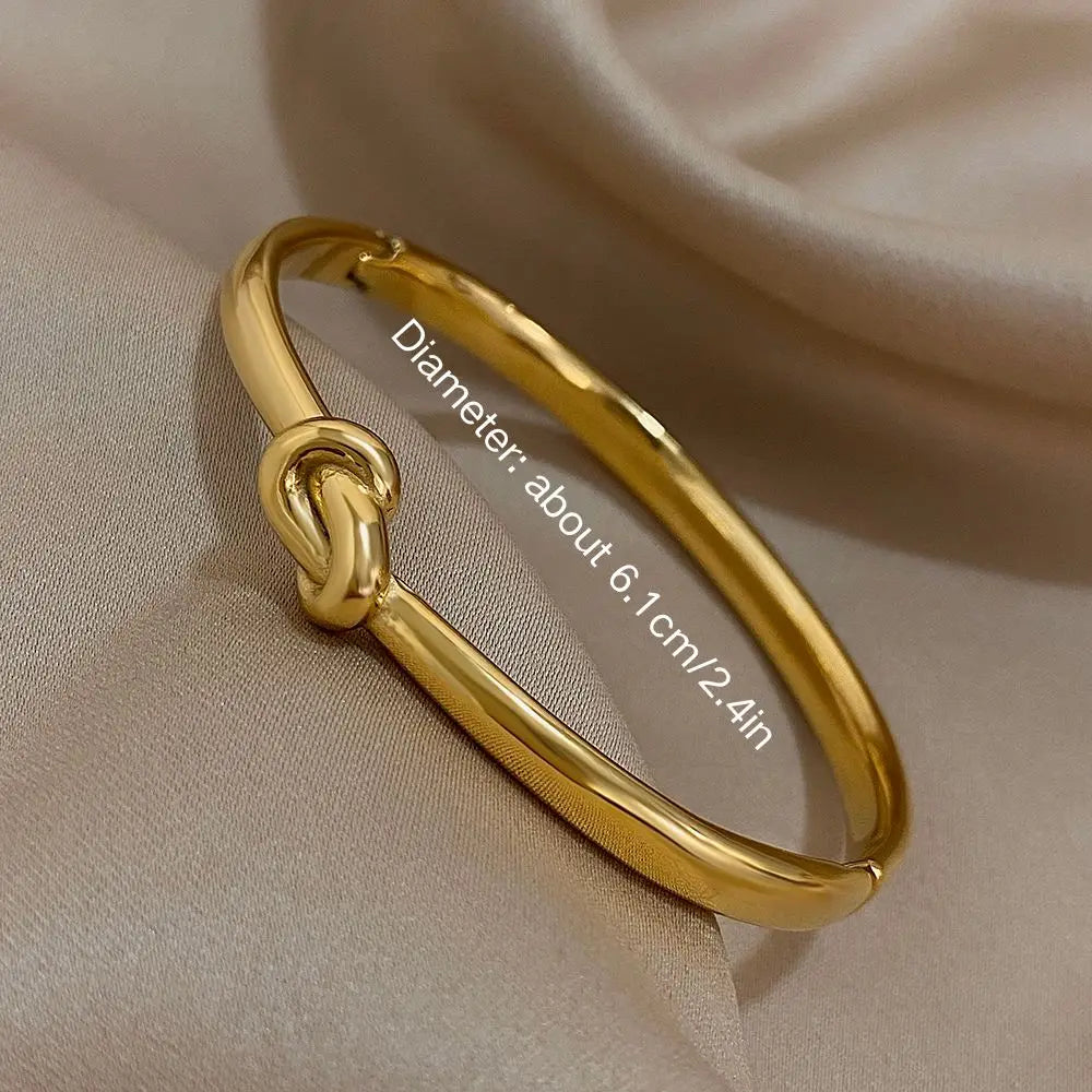 Simple thin stainless steel knotted bangle in gold color displayed on soft satin fabric.